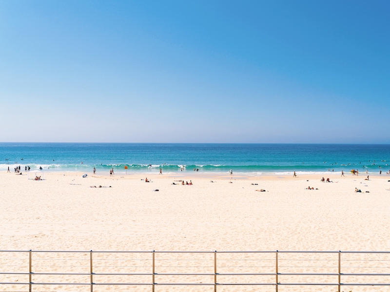 Vue de face d'une plage avec des touristes prenant un bain de soleil, nageant, surfant et se relaxant sur la plage de Bondi à Sydney, Australie, en vacances en été.