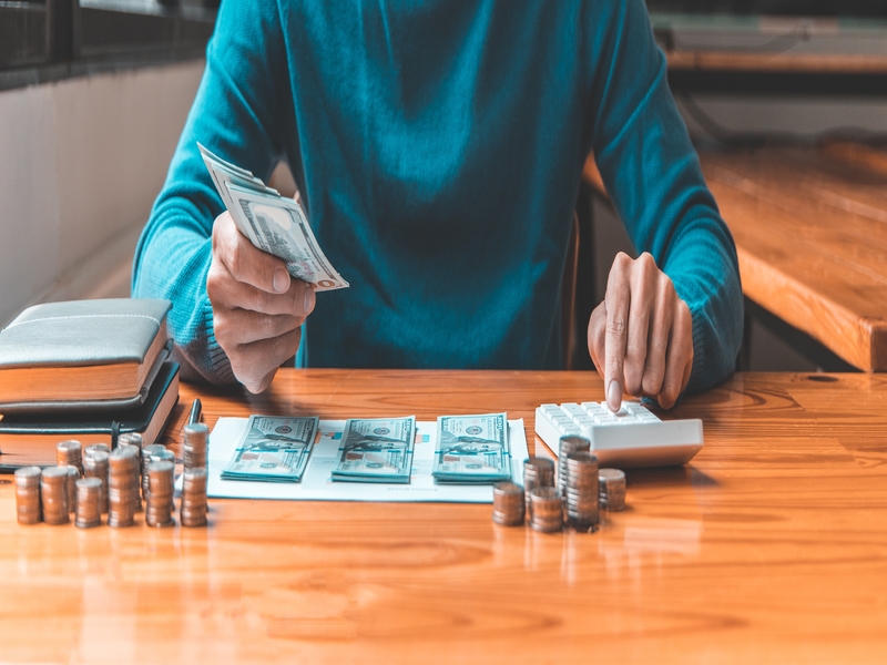 Un homme appuie sur une calculatrice pour calculer le montant qu'il a accumulé au cours de l'année, main tenant un billet d'un dollar, épargner de l'argent pour l'avenir, investissement commercial, finance et comptabilité.