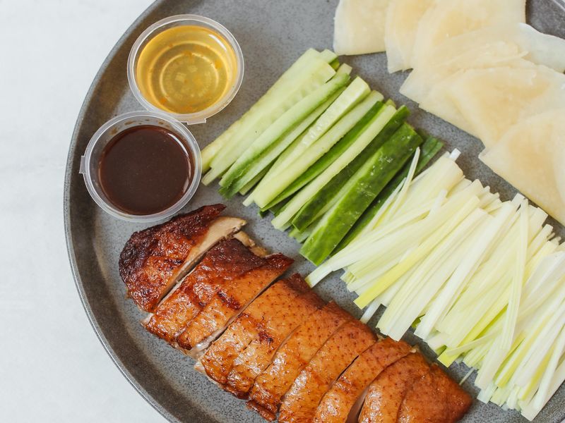 Ici, des légumes en dés et du gingembre en tranches sont posés sur une assiette grise à côté de morceaux de canard rôti de Pékin.
