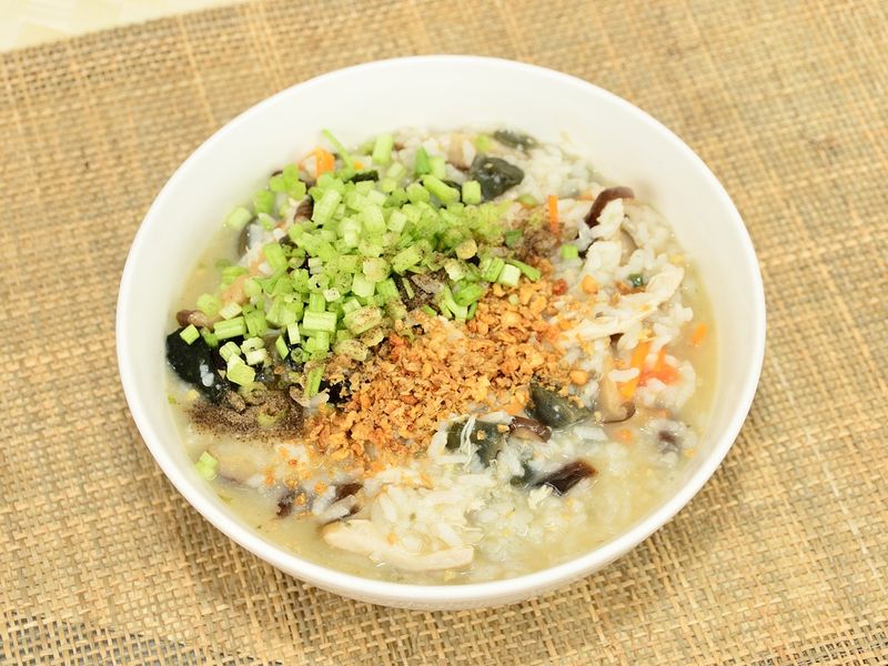 Un bol de congee est posé sur un tissu en toile, avec des légumes écrasés et des oignons frits comme garniture.
