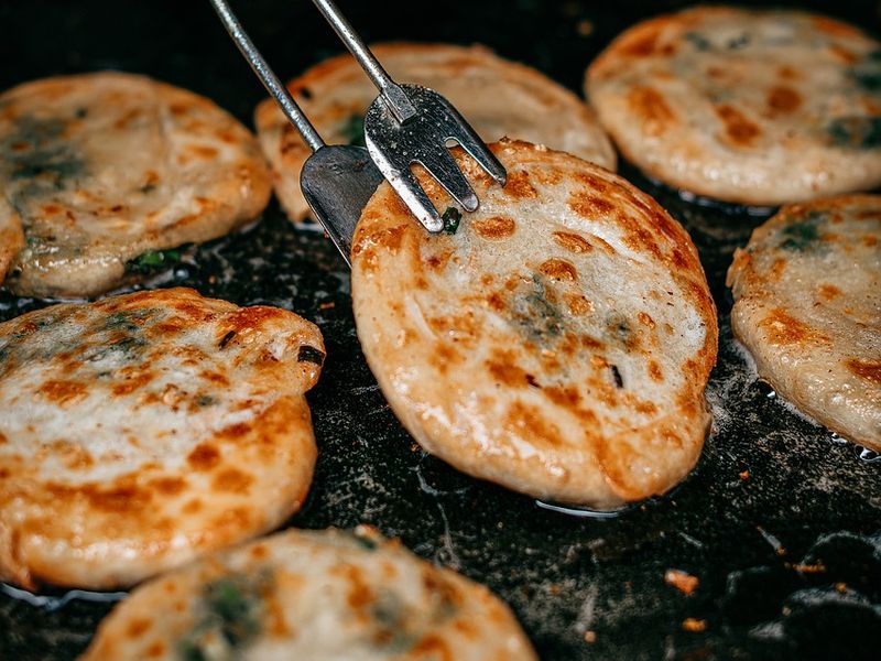 Une fourchette à barbecue soulève une crêpe aux oignons d'une poêle grésillante où d'autres cuisent.