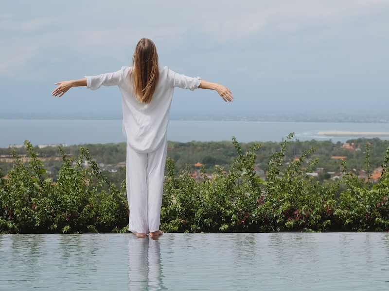 Vue de dos d'une élégante fille en pyjama blanc au bord d'une piscine dans une villa avec une vue imprenable sur Bali.
