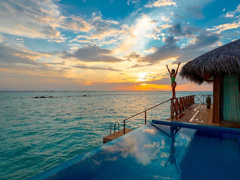 Choisir entre Aruba et les Bermudes ? L'hébergement de luxe est un facteur important. Cette image montre une femme debout près du bord d'une hutte océanique privée.