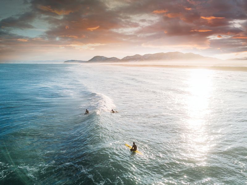 Trois surfeurs attendant de prendre une vague avec une plage étendue en toile de fond.