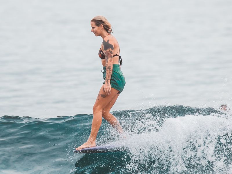 Une femme blonde tatouée attrape une vague douce. Playa Punta Conejo est l'une des meilleures plages de surf au Mexique pour les débutants.