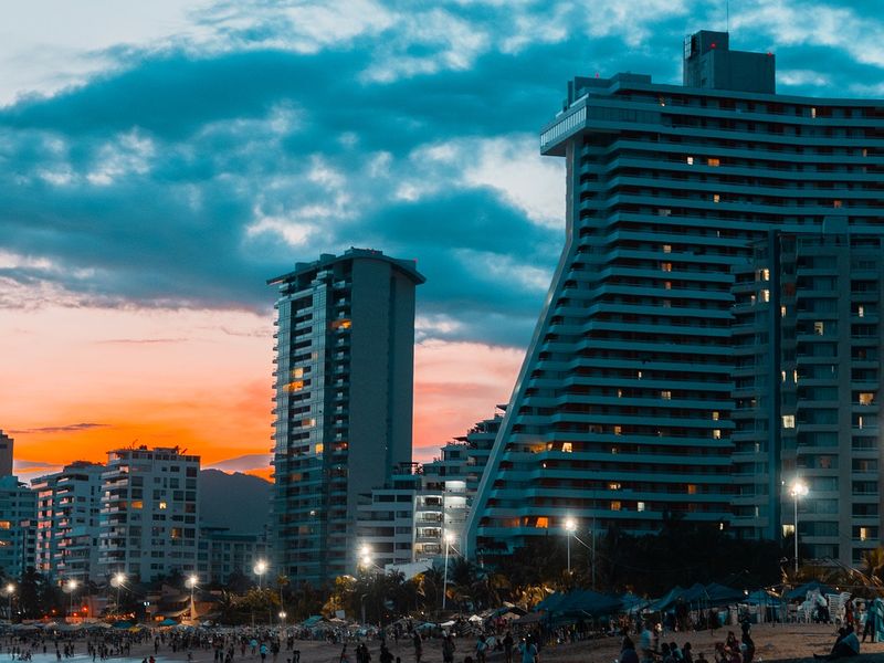 Des bâtiments modernes se trouvent au bord de la plage et les gens s'y promènent au coucher du soleil. 