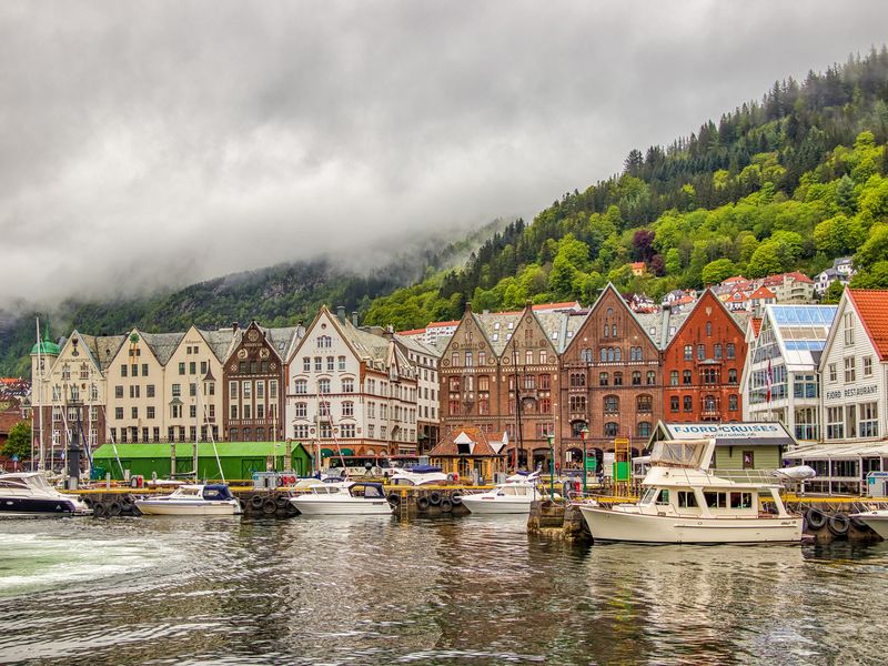 Cette image montre un quai, avec des bateaux amarrés le long du front de mer d'un village norvégien classique.