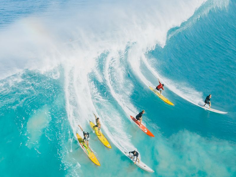 Un groupe de surfeurs attrapant tous la même vague dans une mer bleu clair. Les nombreux moniteurs et camps de surf de Playa Tamarindo en font un bon spot de surf pour les débutants au Costa Rica.