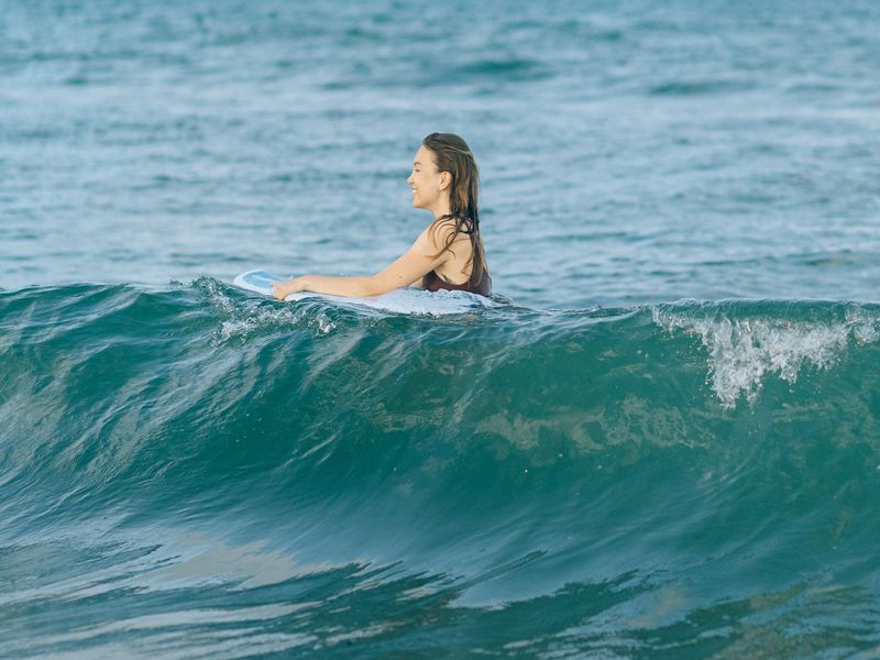Une femme se tient dans l'eau en riant avec une planche de surf. Les eaux calmes de Playa Samara permettent aux débutants de faire du surf au Costa Rica.