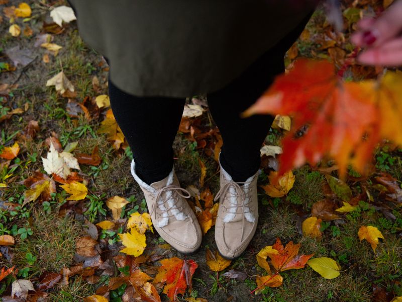 Ici, une photo montre le bas d'une jambe d'une fille avec des feuilles d'automne en arrière-plan.