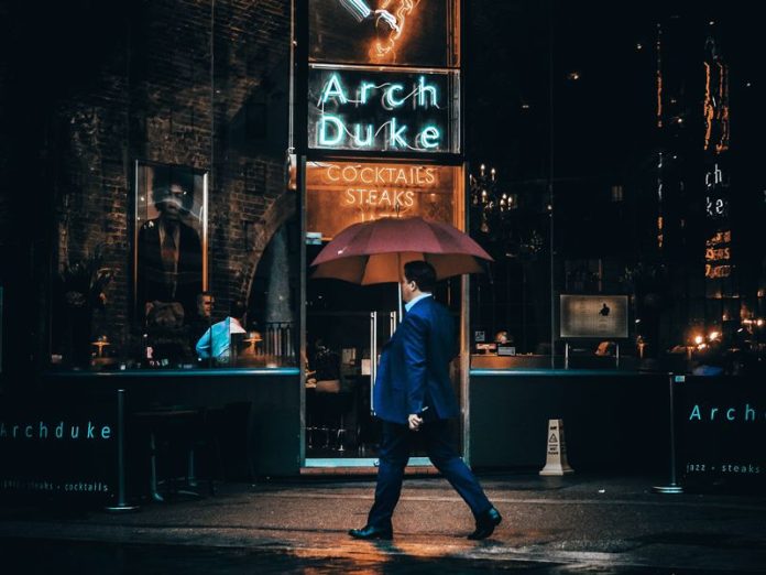 La culture vestimentaire britannique couvre une grande variété de catégories de vêtements. Ici, un homme seul en costume passe devant un bar avec un parapluie.